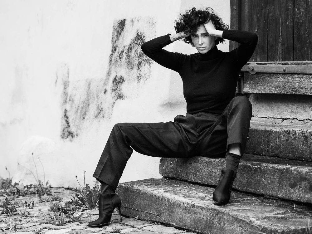 Black and white photo of a stylish woman sitting on outdoor steps posing.