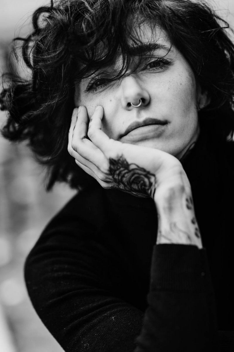 Black and white portrait of a person with nose ring and hand tattoo resting chin on hand.