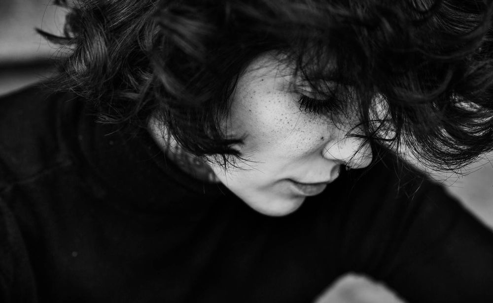 Black and white close-up portrait of a curly-haired woman looking downward.