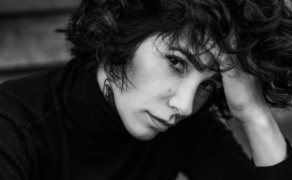 Moody black and white close-up portrait of a person with short dark hair resting head on hand.