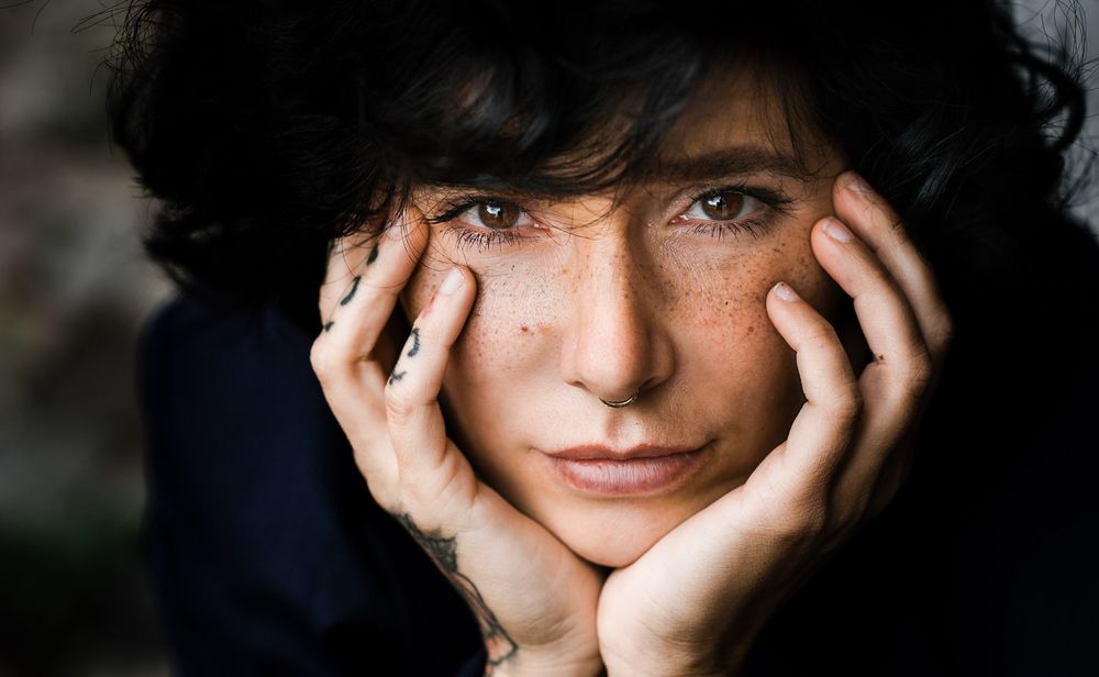 Close-up portrait of a woman with freckles resting her face in her hands.