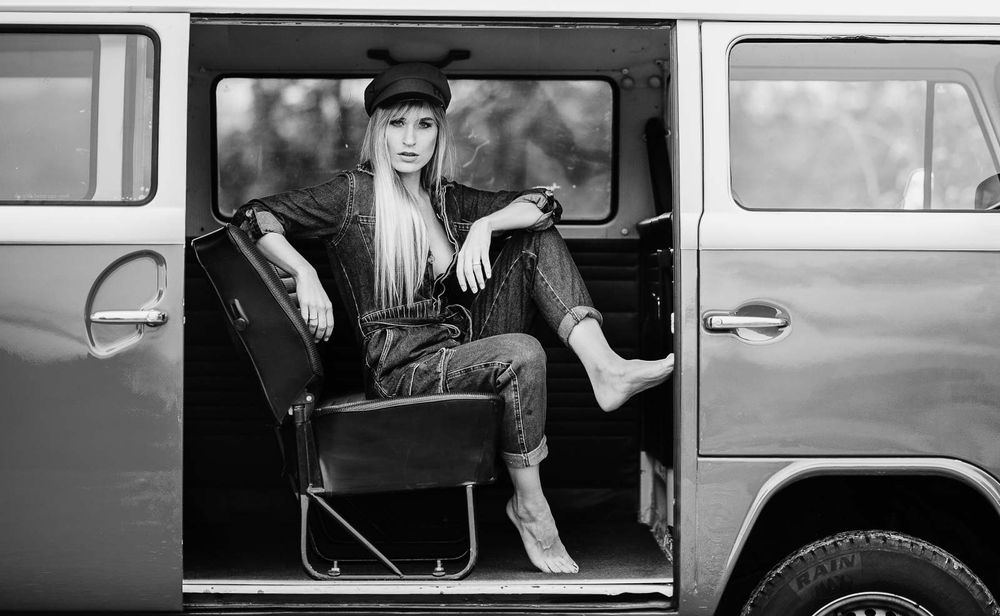 Woman in black cap sits in vintage VW bus doorway, black and white photo.