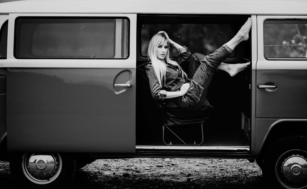 Blonde woman relaxes with legs up in vintage VW bus doorway, black and white.