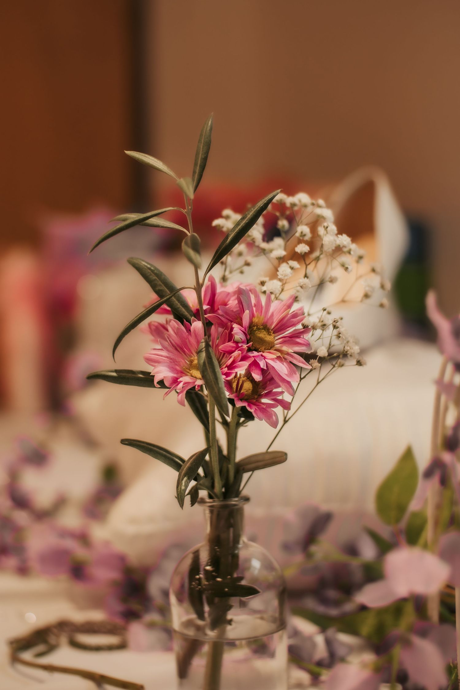 Pink daisy flowers in a small glass vase with delicate table decorations.