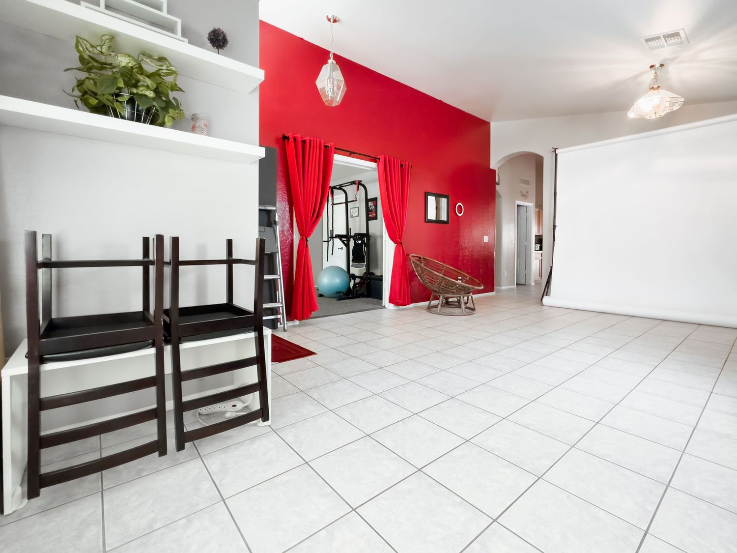 Modern room interior with red accent wall, white tile floor and dark wooden chairs.