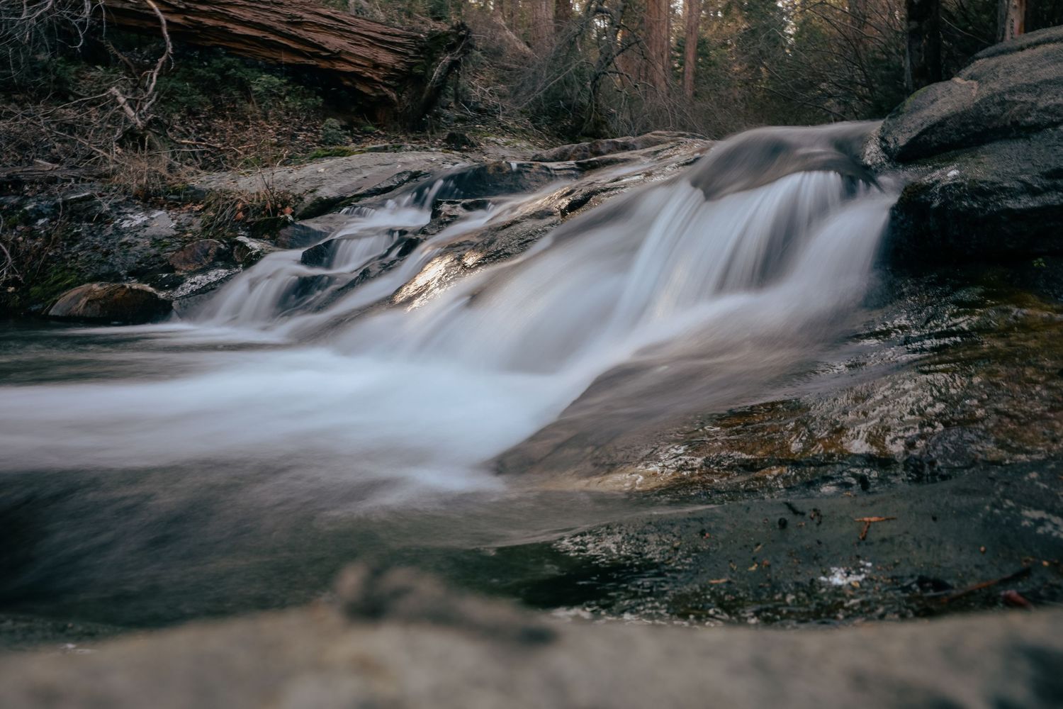 Long exposure waterfall flowing over rocks in a forest stream with silky smooth water effect.