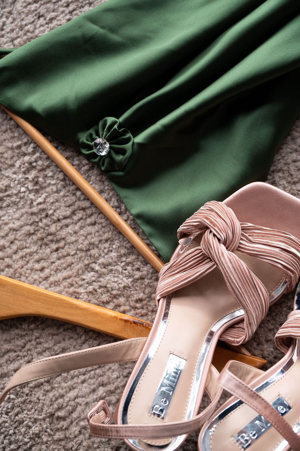 Pink strappy sandals and green fabric on gray carpet with wooden hangers, creating a stylish fashion composition.