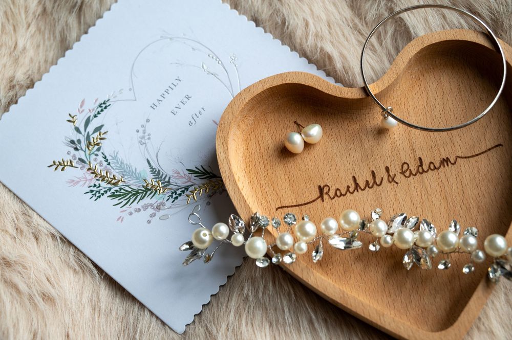 Wedding invitation and wooden heart-shaped dish with delicate floral accents on a textured fabric background.