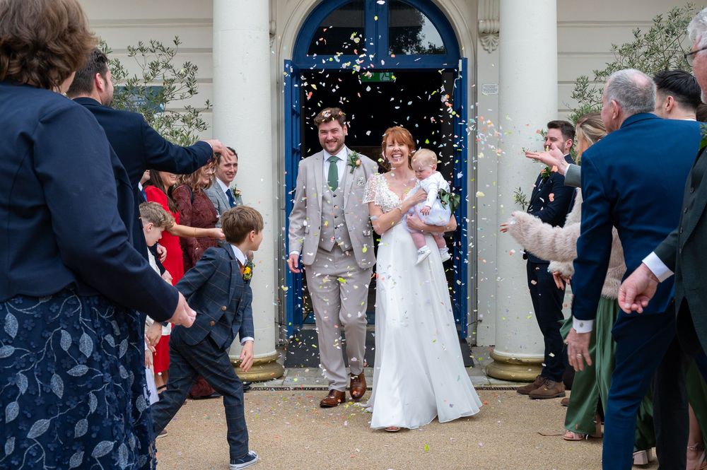 Guests throw confetti over a couple exiting through a blue church doorway after their wedding ceremony.