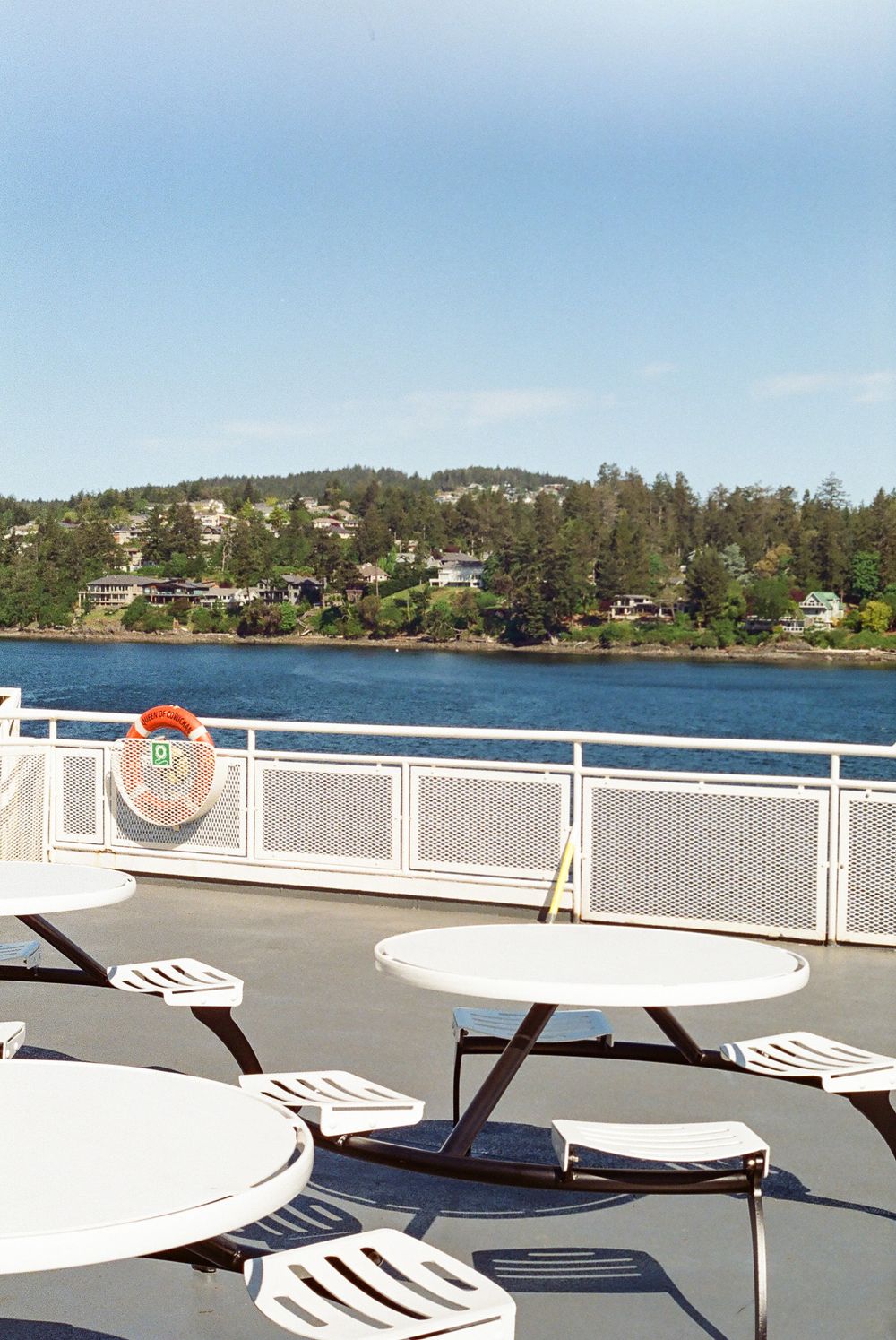 White tables and chairs on ferry deck overlooking waterfront scenery.