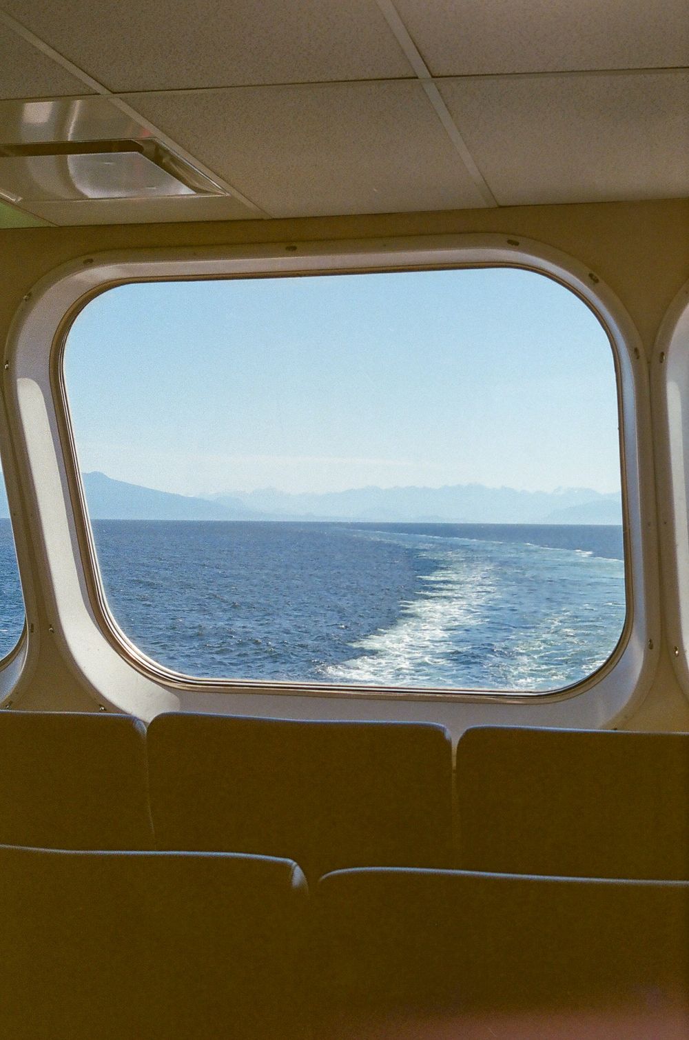 View of ocean waves through ferry windows showing wake and distant coastline.