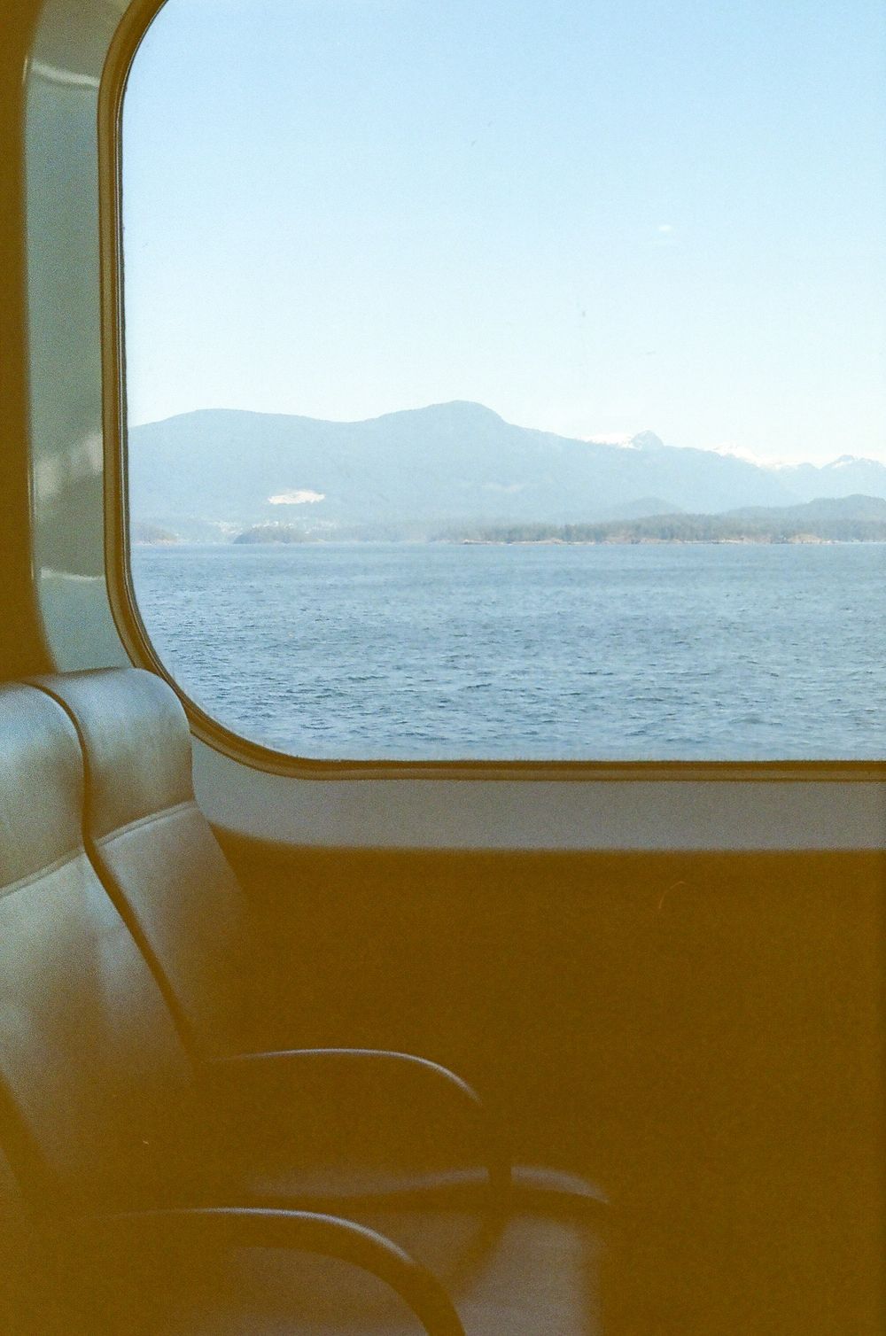 View of distant mountains and water through ferry windows with passenger seats visible in the foreground.