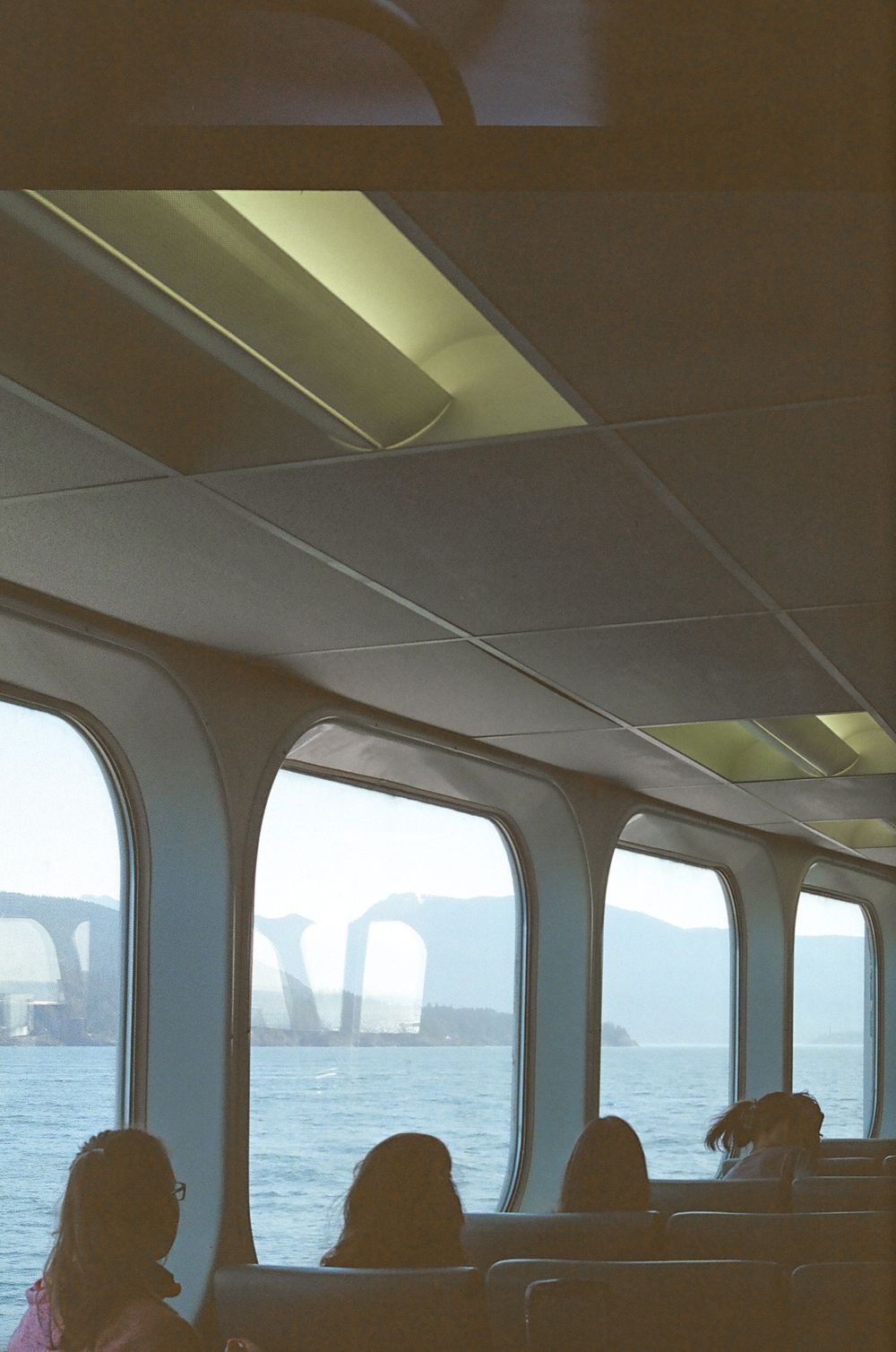 Inside view of a ferry cabin with windows showing water and mountains in the distance.