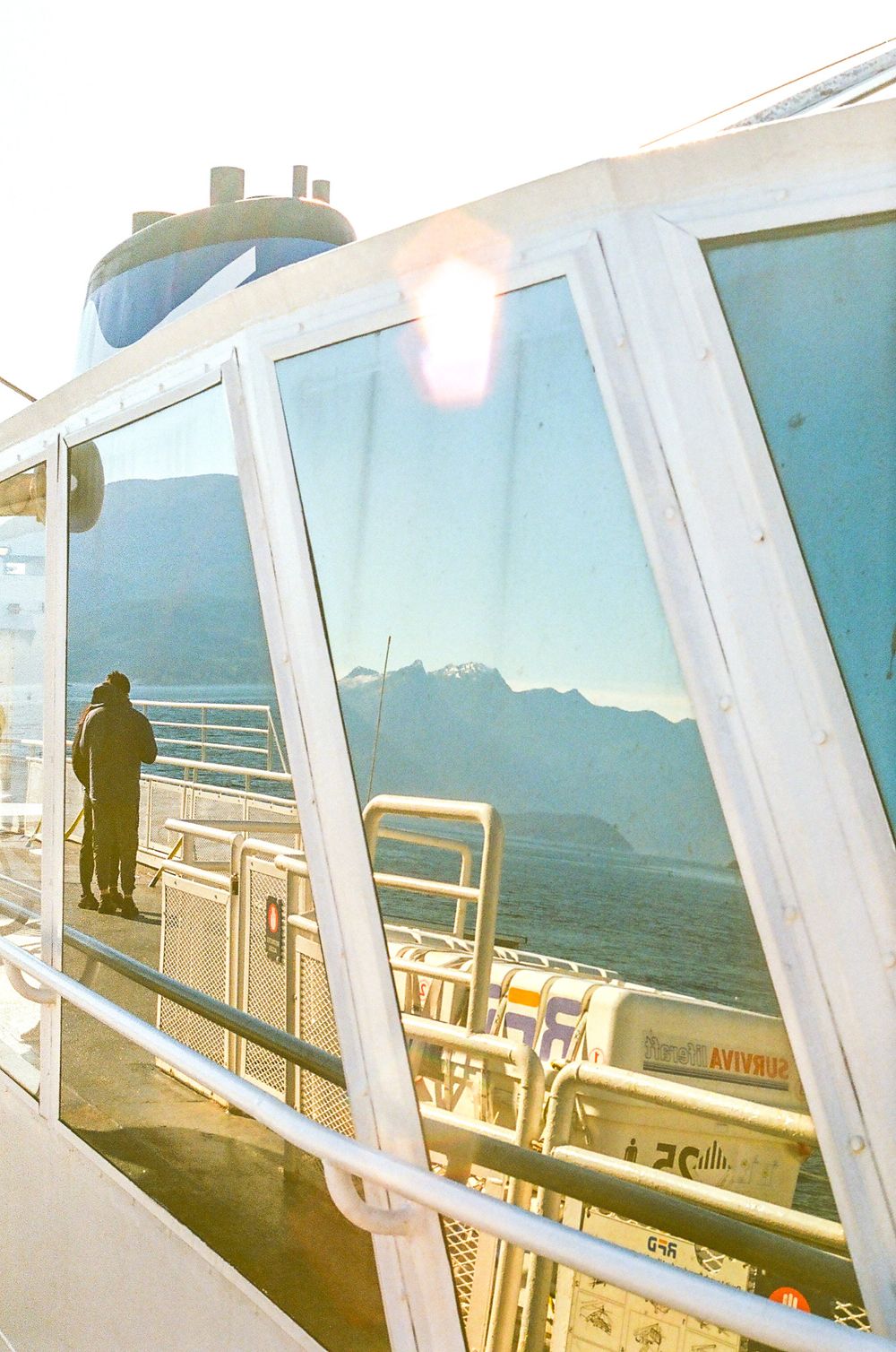 Passenger deck of a ferry with large windows overlooking mountain scenery.