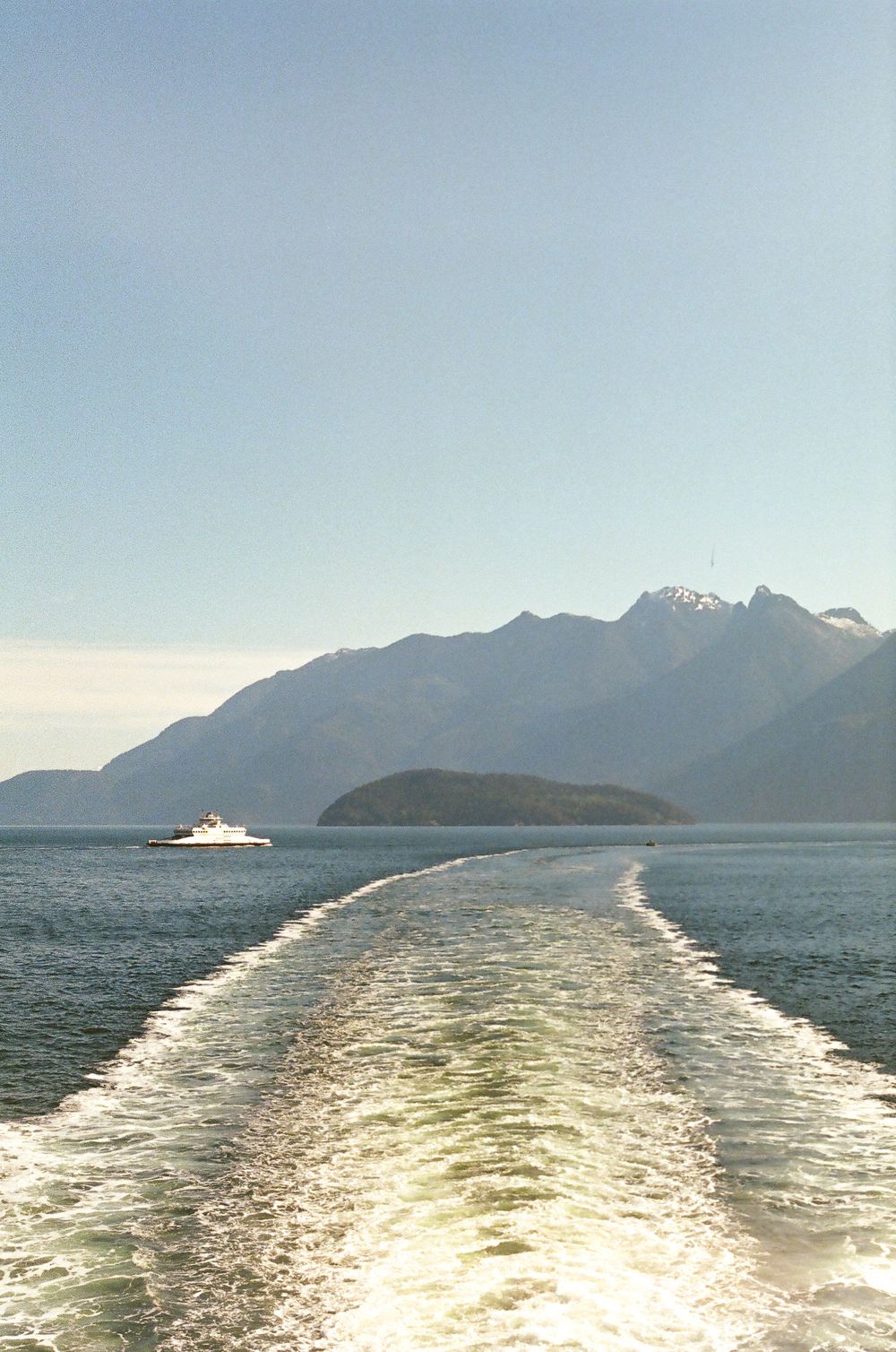 Wake pattern behind a ferry boat crossing mountain-lined waters on a sunny day.