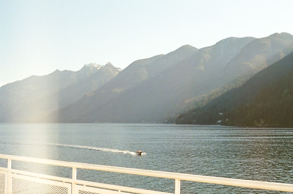 Scenic mountain lake view from a boat deck with sun glare and distant peaks in the background.