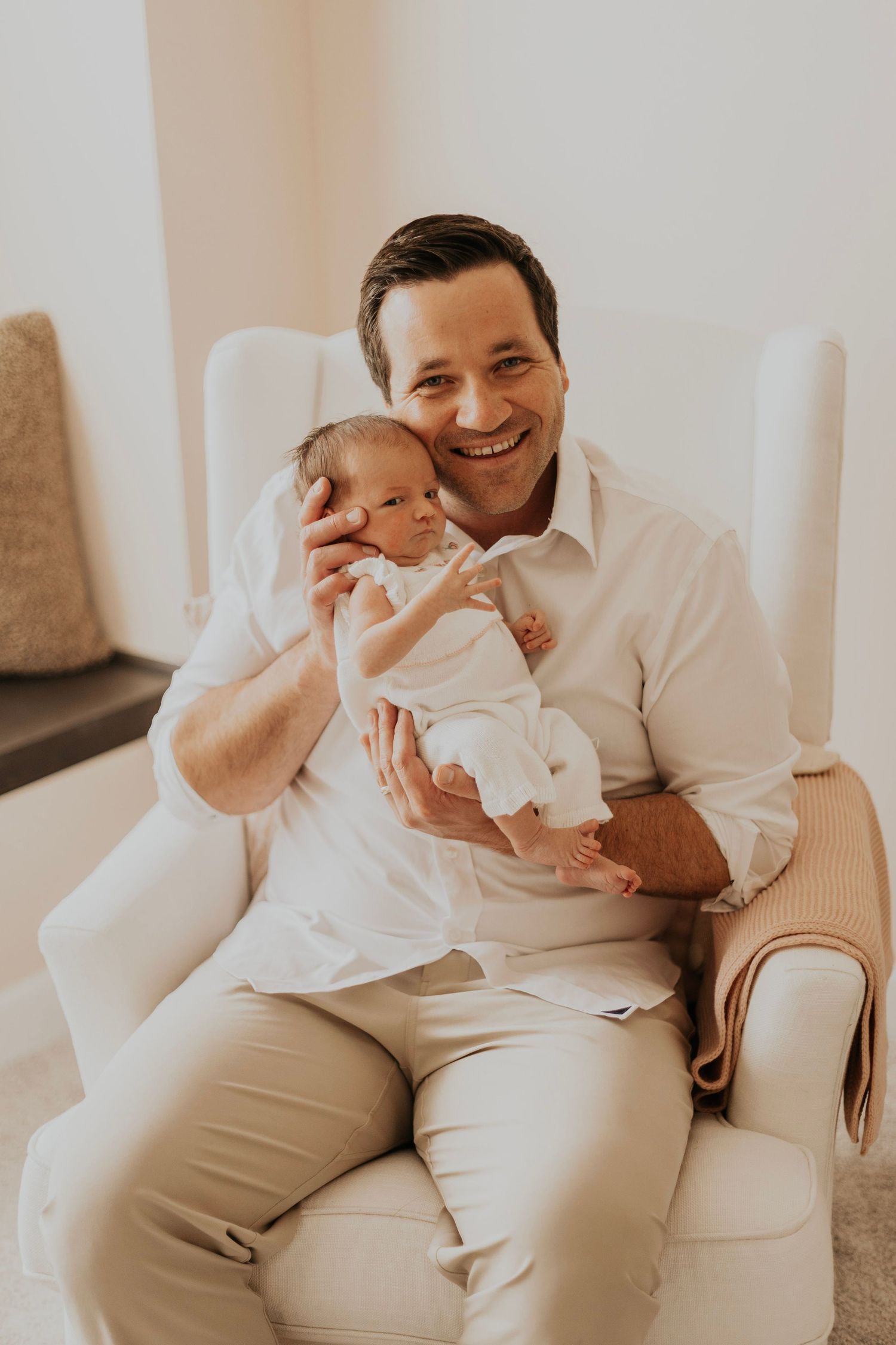 A joyful moment captured as a parent holds their newborn baby in a cozy armchair.