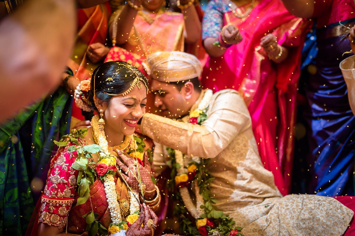 A couple in traditional Indian wedding attire participate in a Haldi ceremony with bright yellow turmeric paste and colorful decorations.
