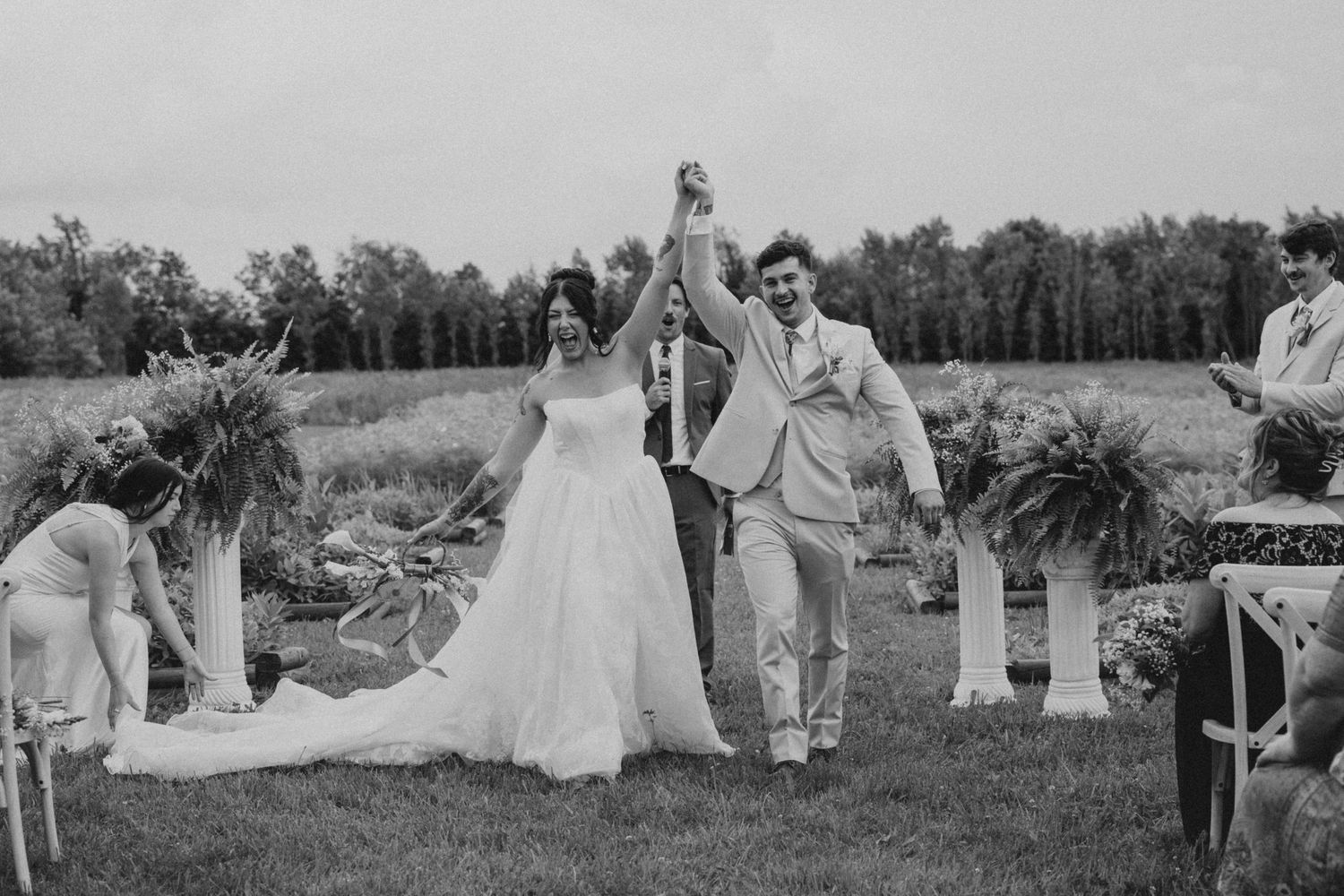A black and white wedding photo capturing a couple's first look reaction by a lakeside.