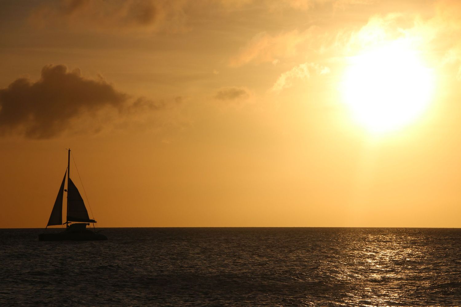 A sailboat silhouetted against a golden sunset over calm ocean waters with dramatic clouds.
