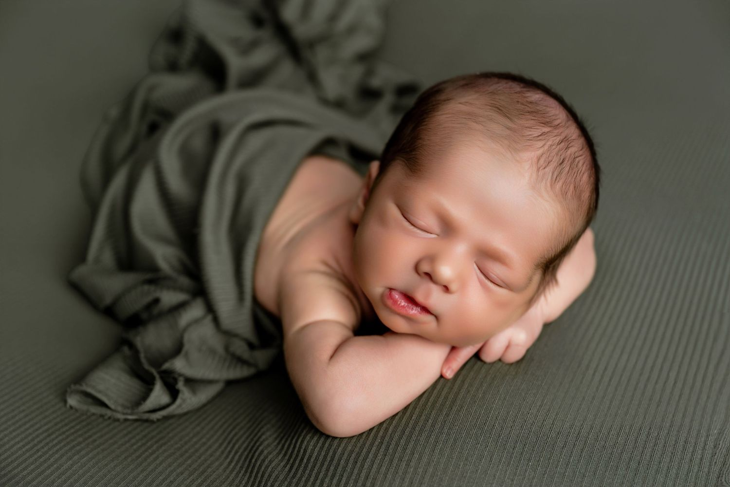 Peaceful newborn baby sleeping on green fabric wrap in a professional newborn photography pose.