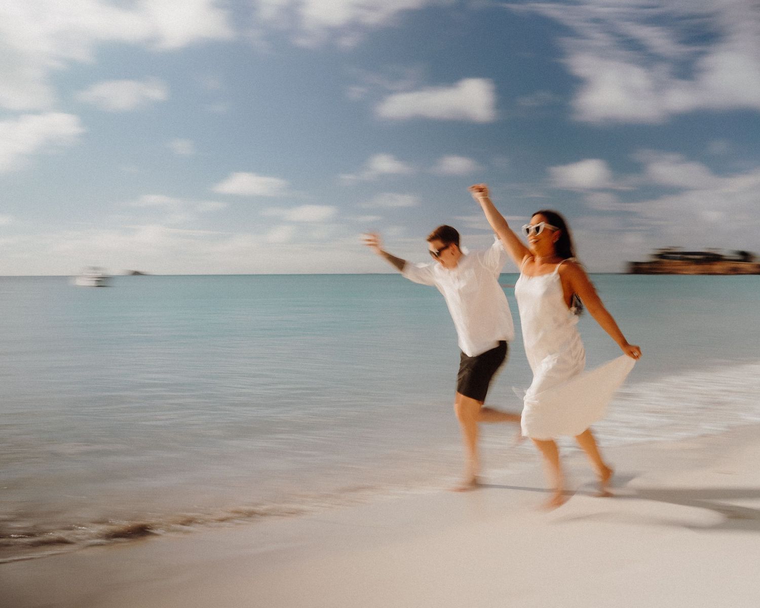 Carefree couple dancing on pristine white sand beach with arms outstretched.