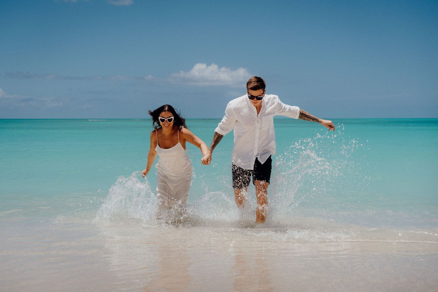Joyful couple splashing in crystal clear turquoise waters on a tropical beach.