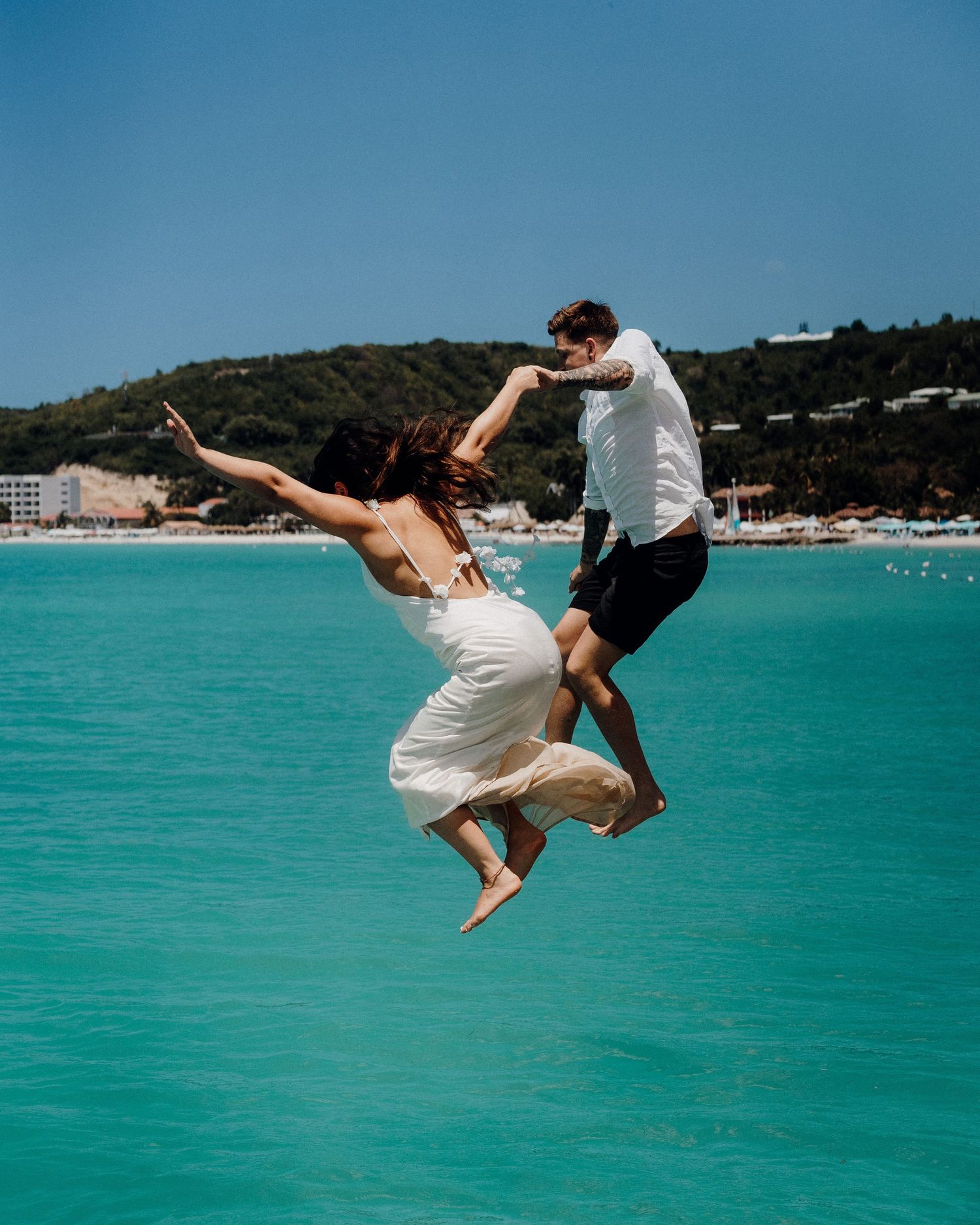 Playful couple jumping into turquoise water at a tropical beach destination.