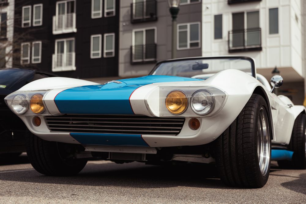 Classic white and blue striped vintage sports car roadster parked on urban street in sunlight.