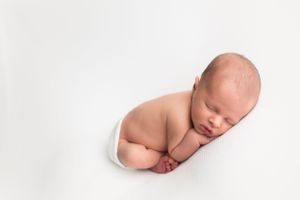 Peaceful newborn baby curled up sleeping on white background in minimal photography style.