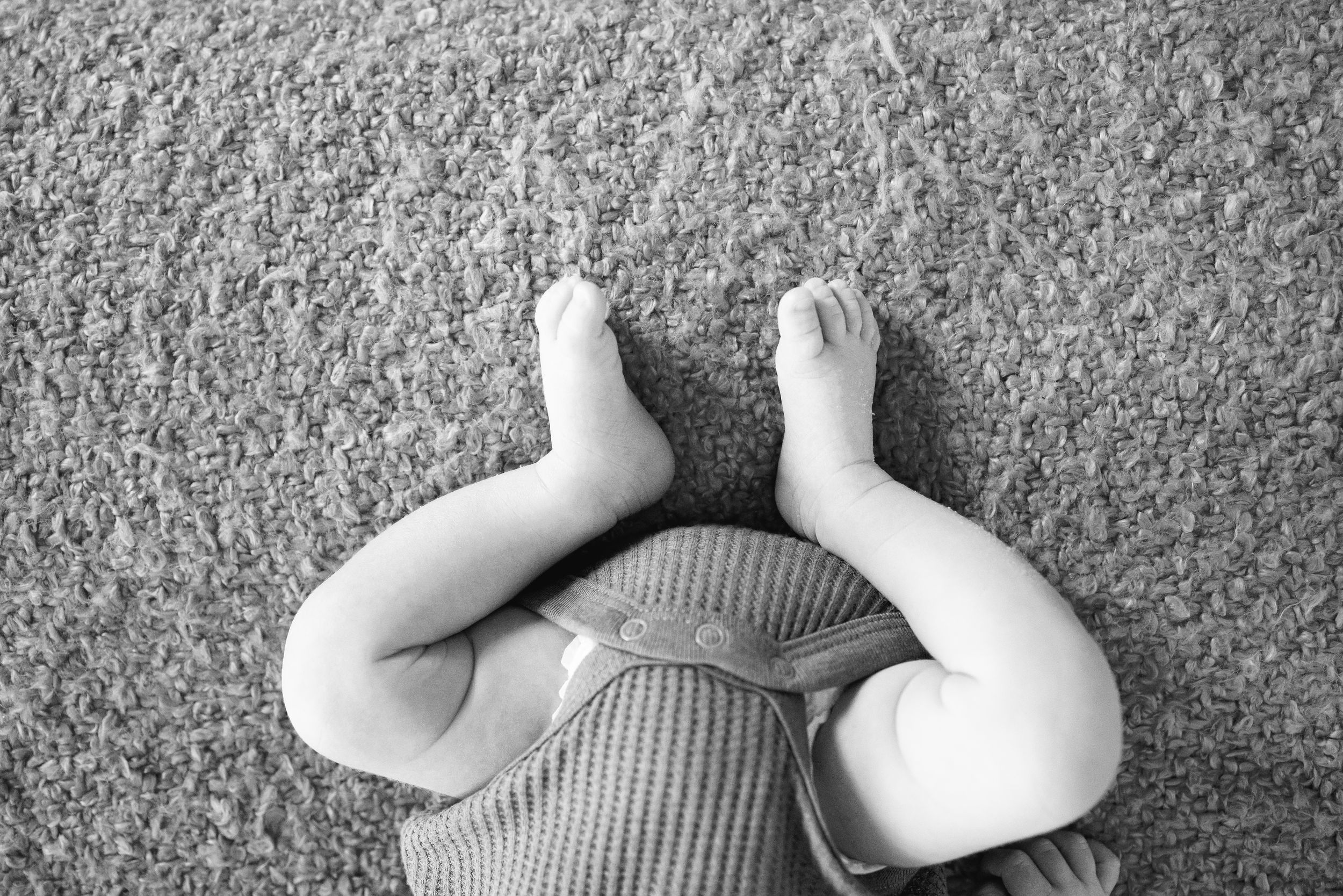 Black and white overhead view of small baby feet against textured carpet.