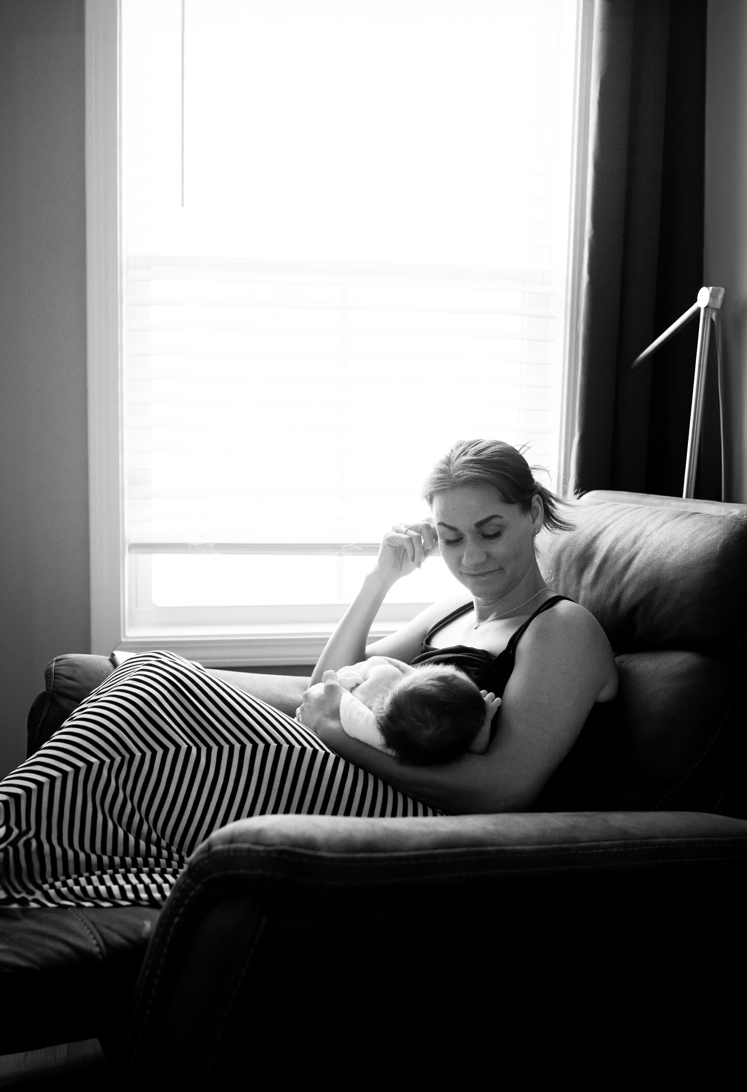 A tender black and white photograph of a peaceful moment between parent and infant on a couch by a window.