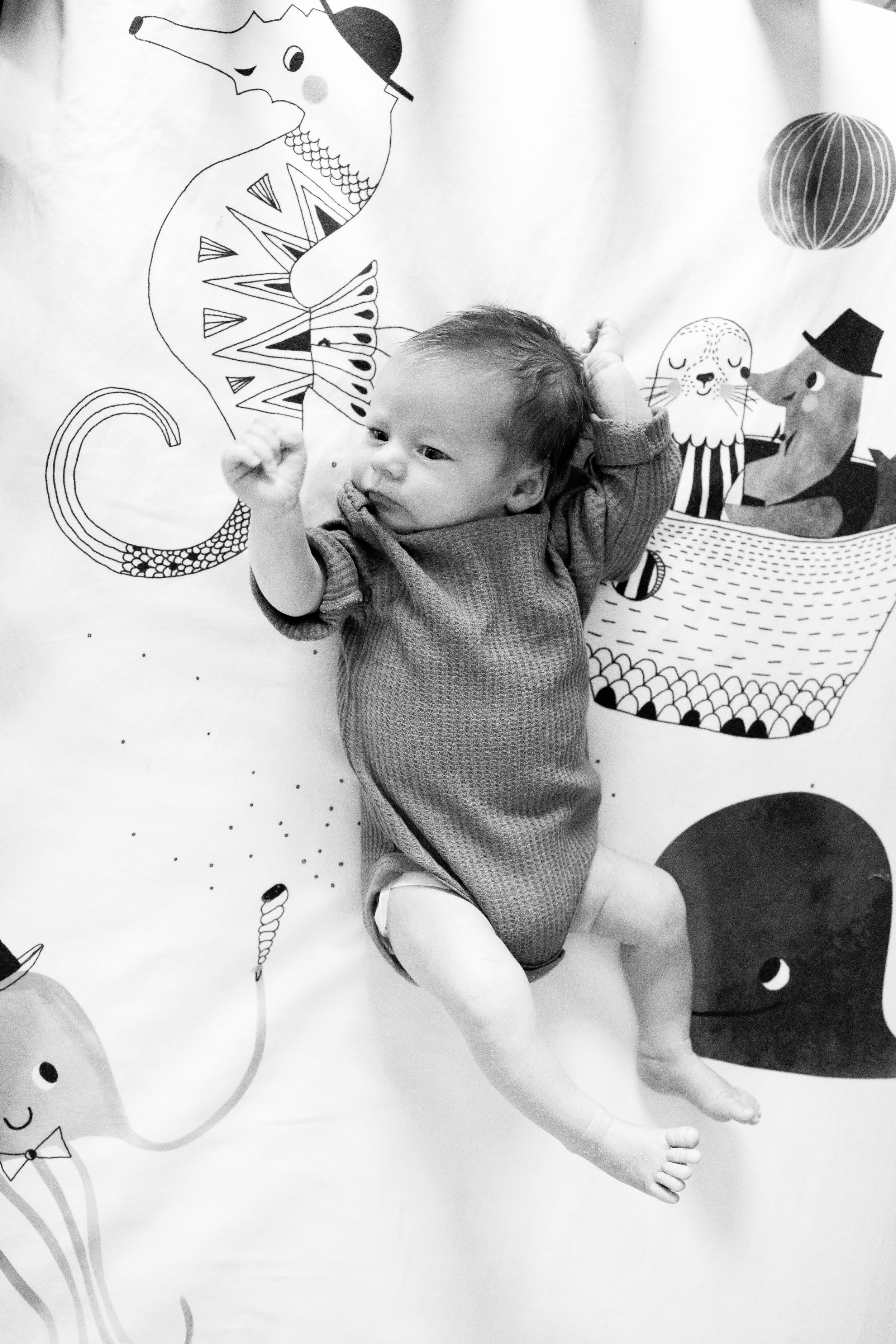 Baby lying on playmat with whimsical animal illustrations in black and white.