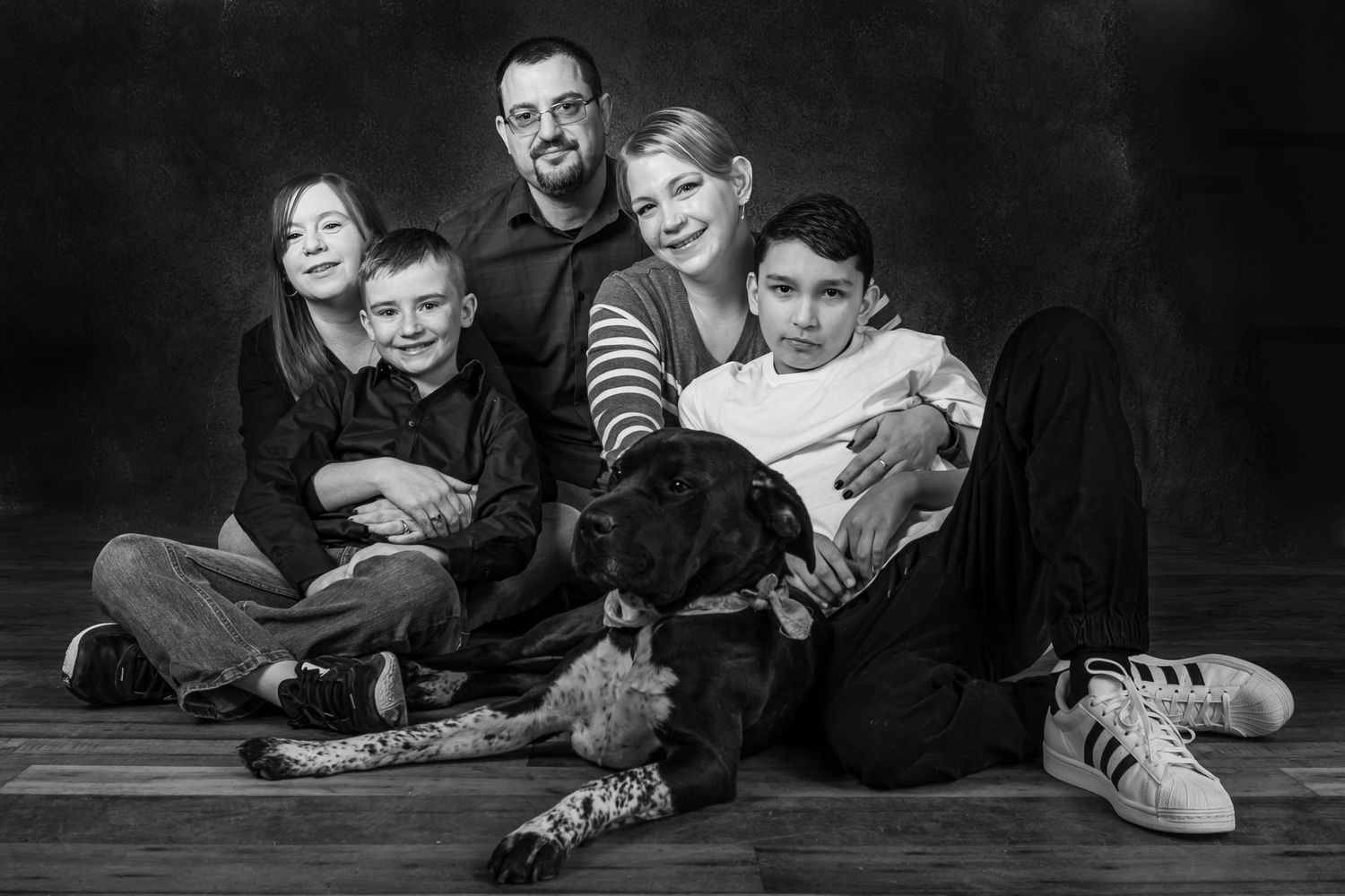 A black and white family portrait on the floor with their pet dog.