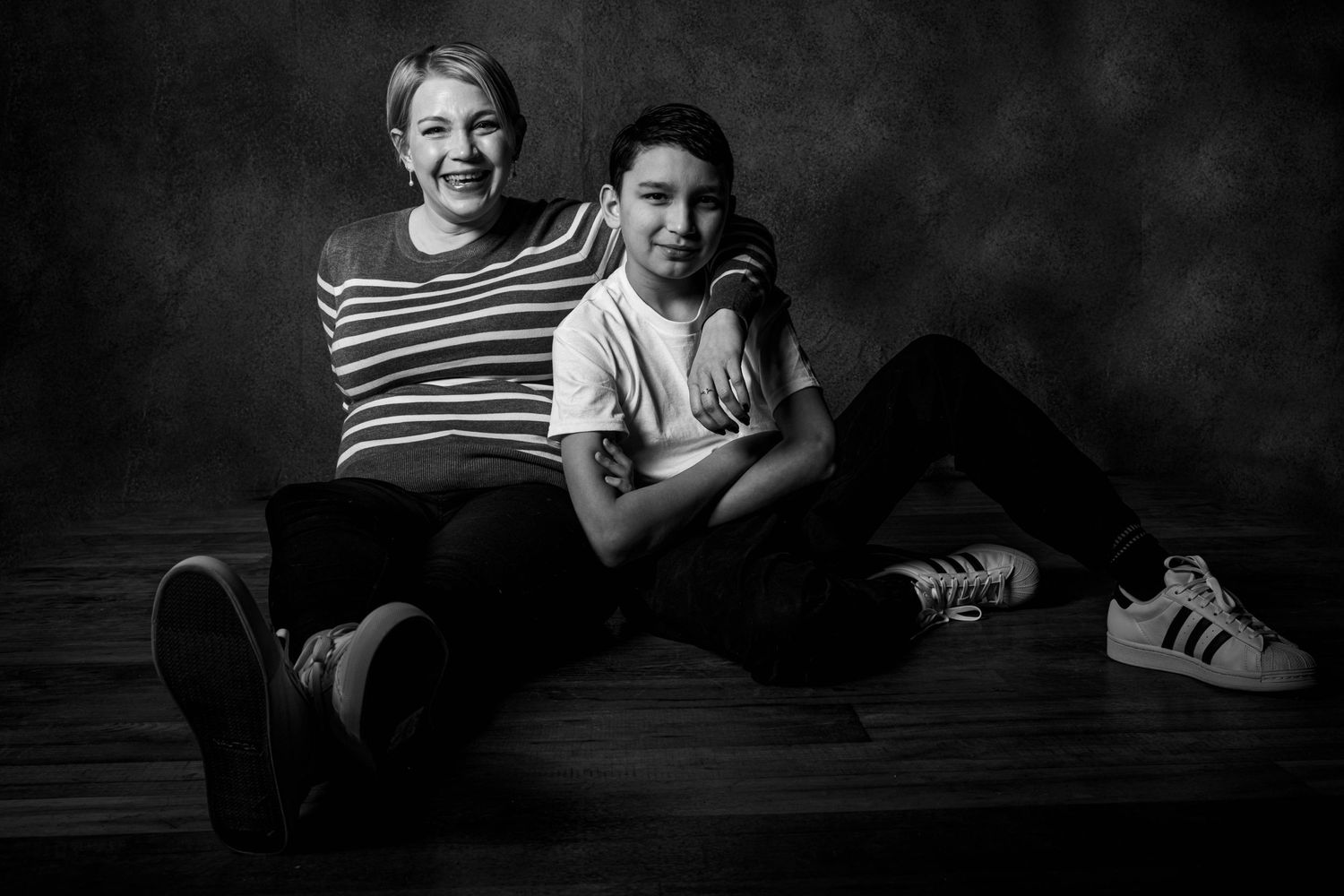 A black and white portrait of two people sitting casually on a dark background.