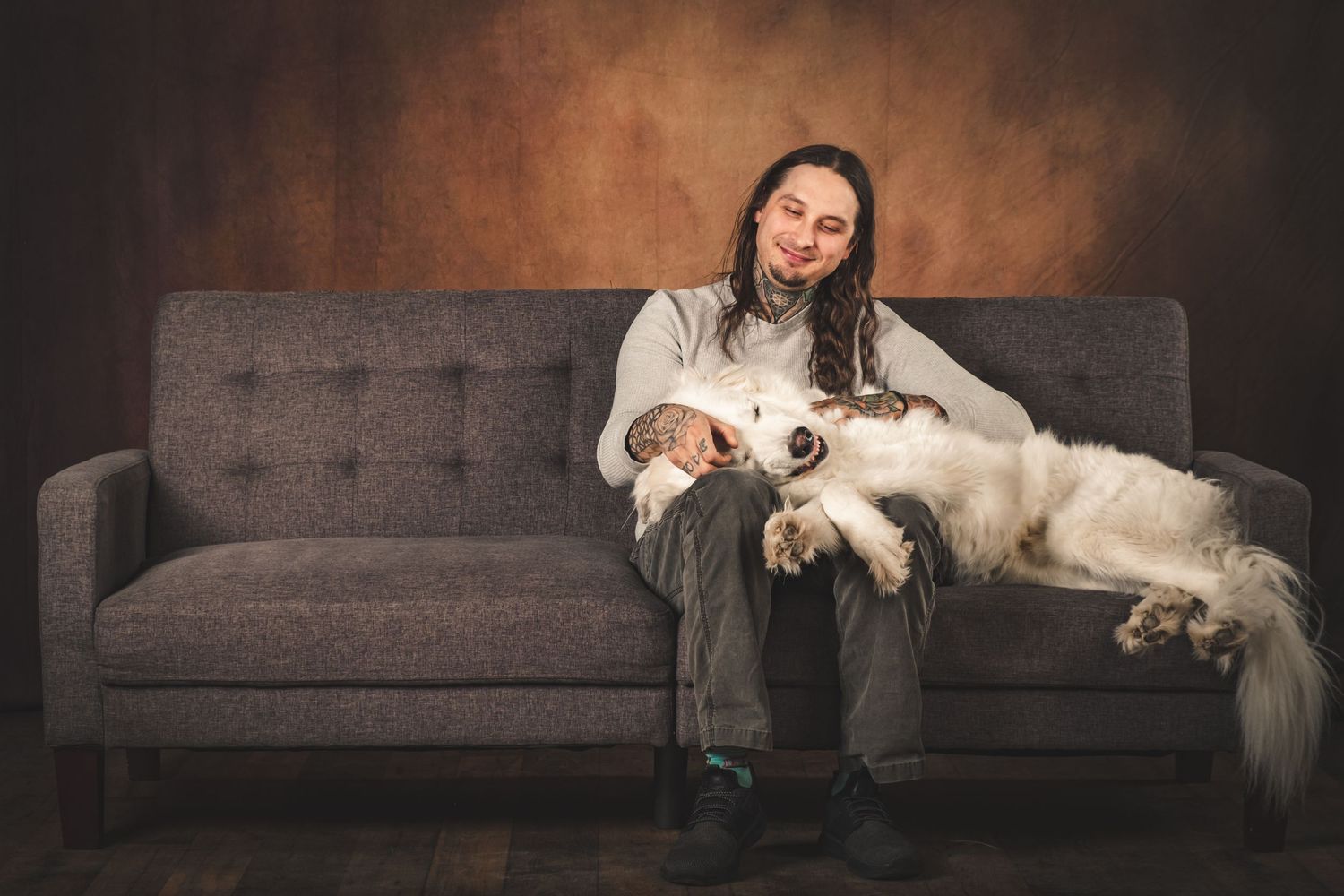 Person relaxing on grey couch with white dog stretched out across their lap. Family Photography