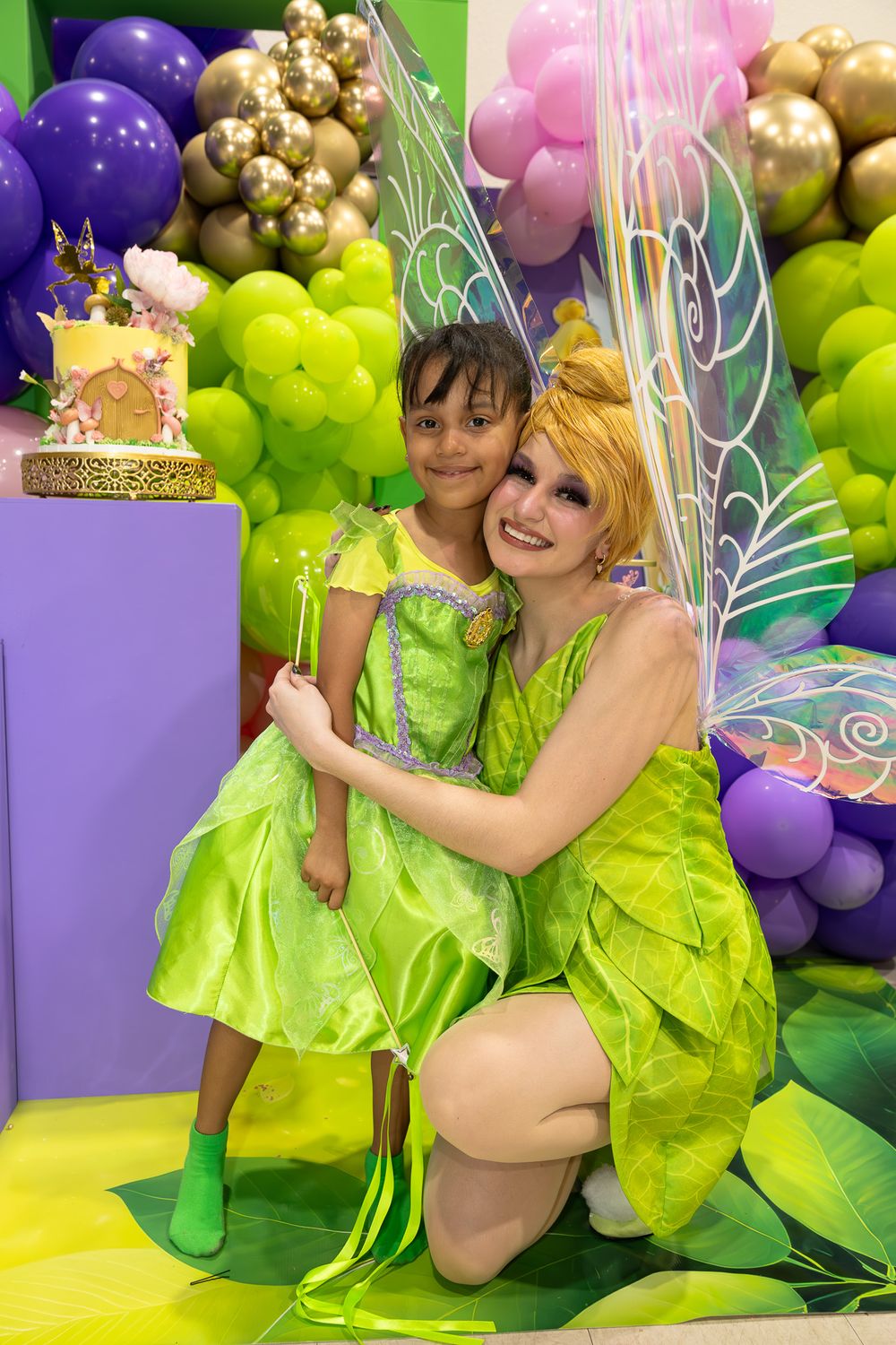 Whimsical fairy-themed party setup with purple and green balloon garlands and decorative wings.