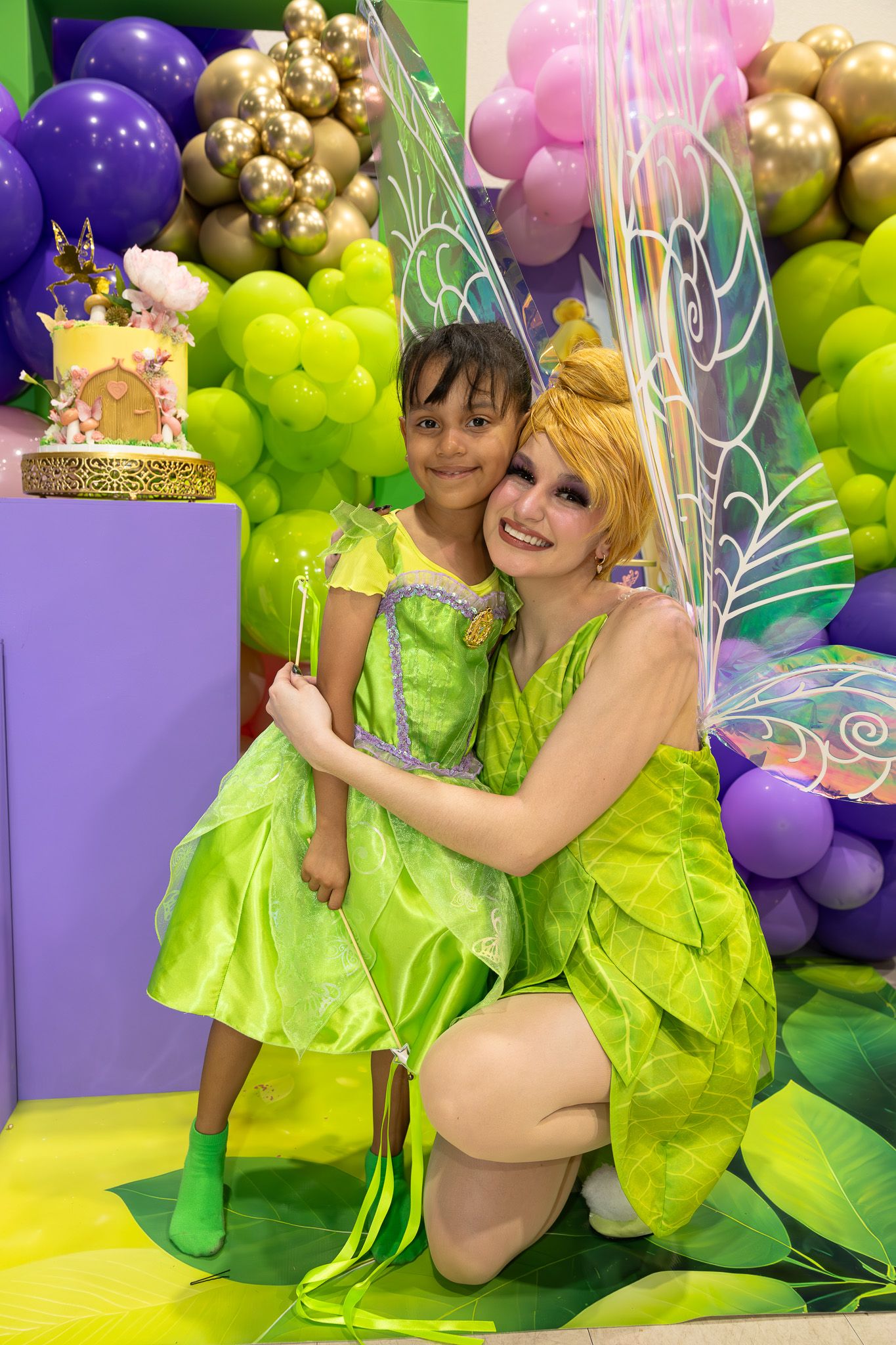 Whimsical fairy-themed party setup with purple and green balloon garlands and decorative wings.