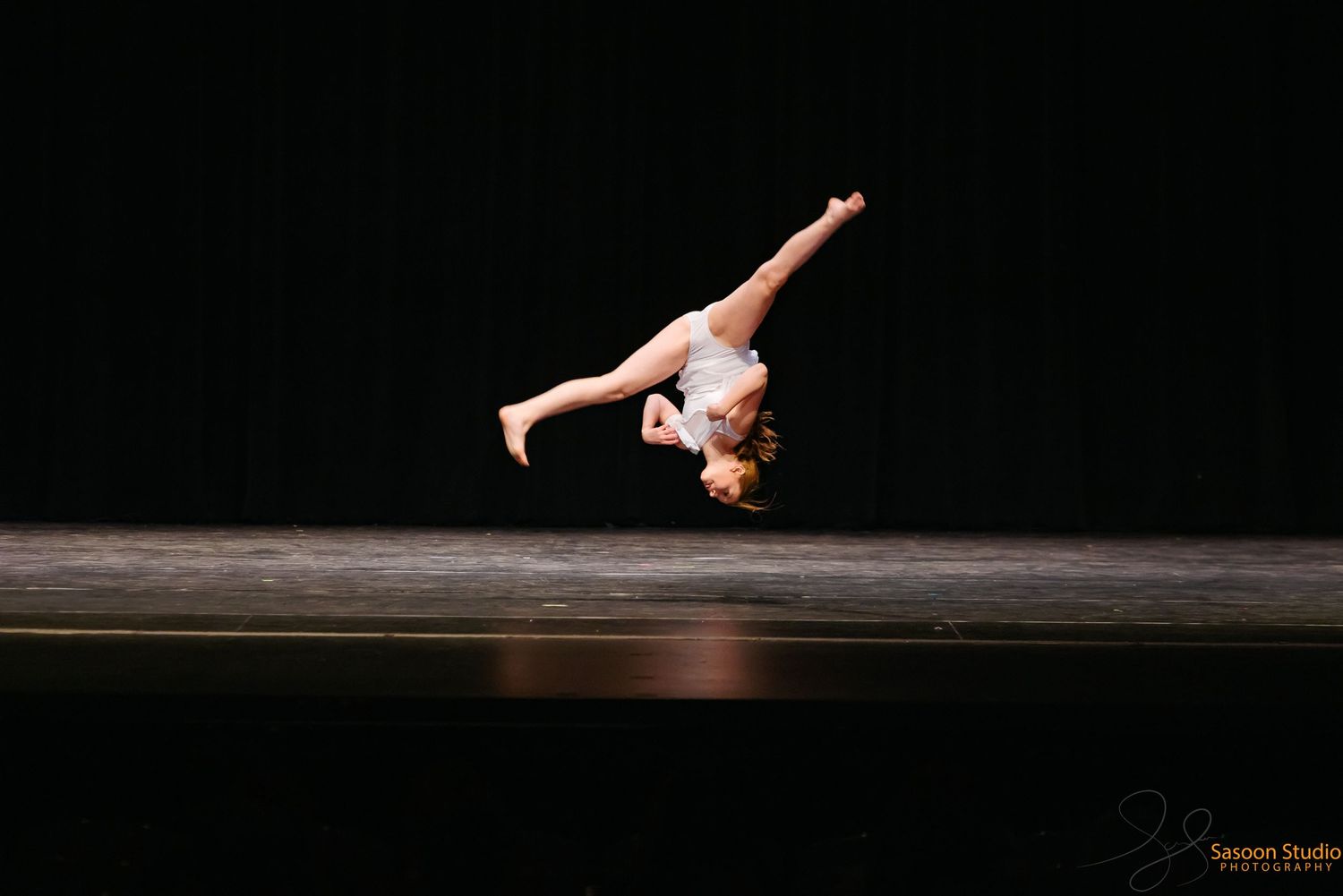 Dynamic dance move showing an aerial cartwheel on dark stage.