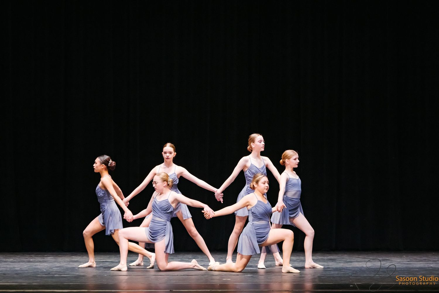 Modern dance ensemble performs synchronized movements in flowing purple costumes.