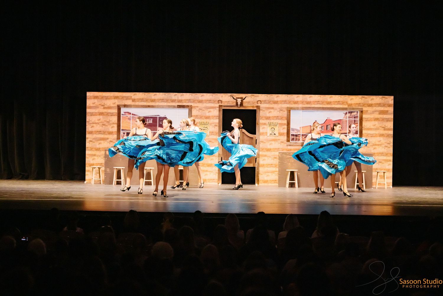 Theater stage set with blue car props against wooden backdrop during performance.