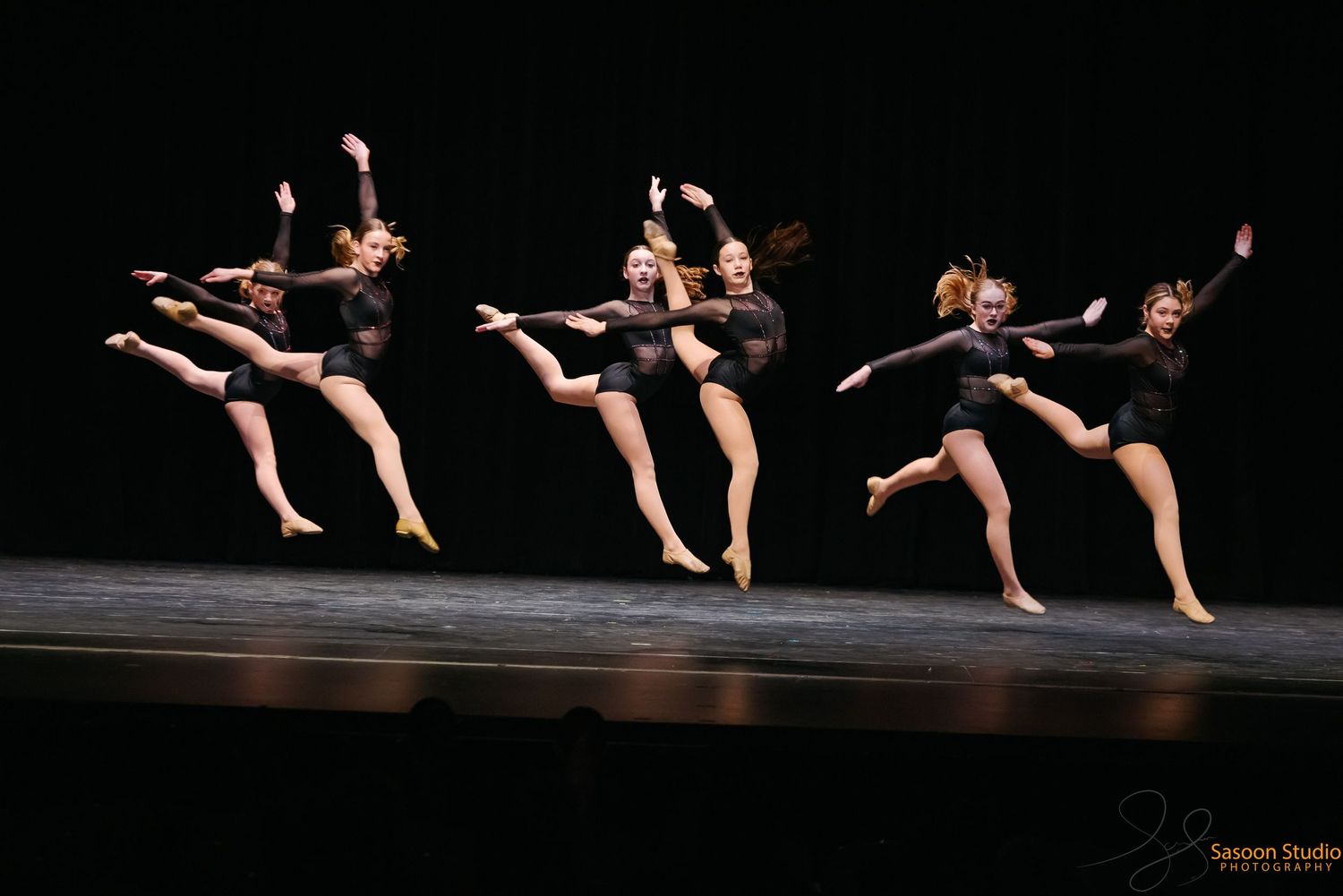 A synchronized dance performance with multiple dancers in black costumes on stage.
