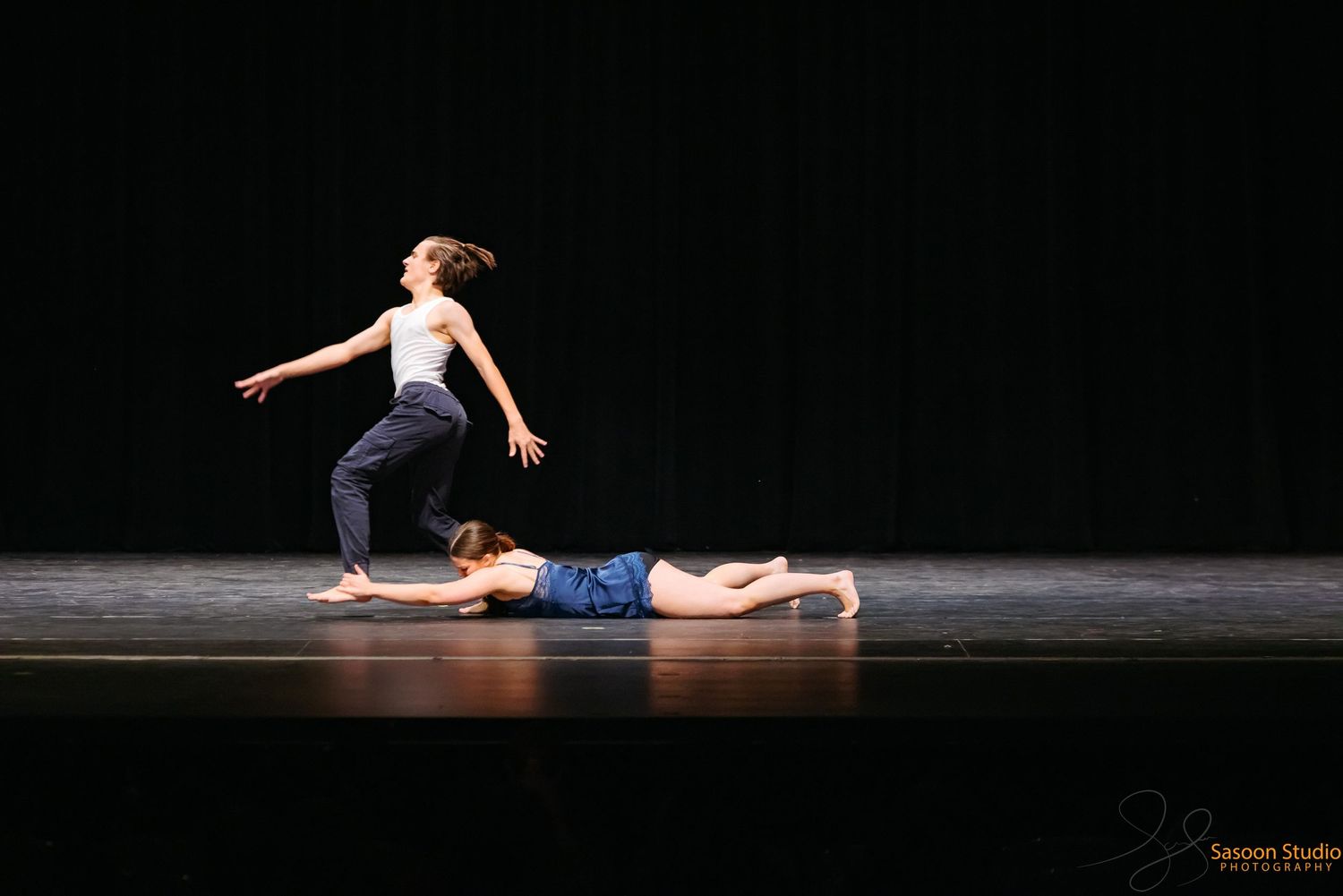 Two dancers perform a contemporary duet on a dark stage.