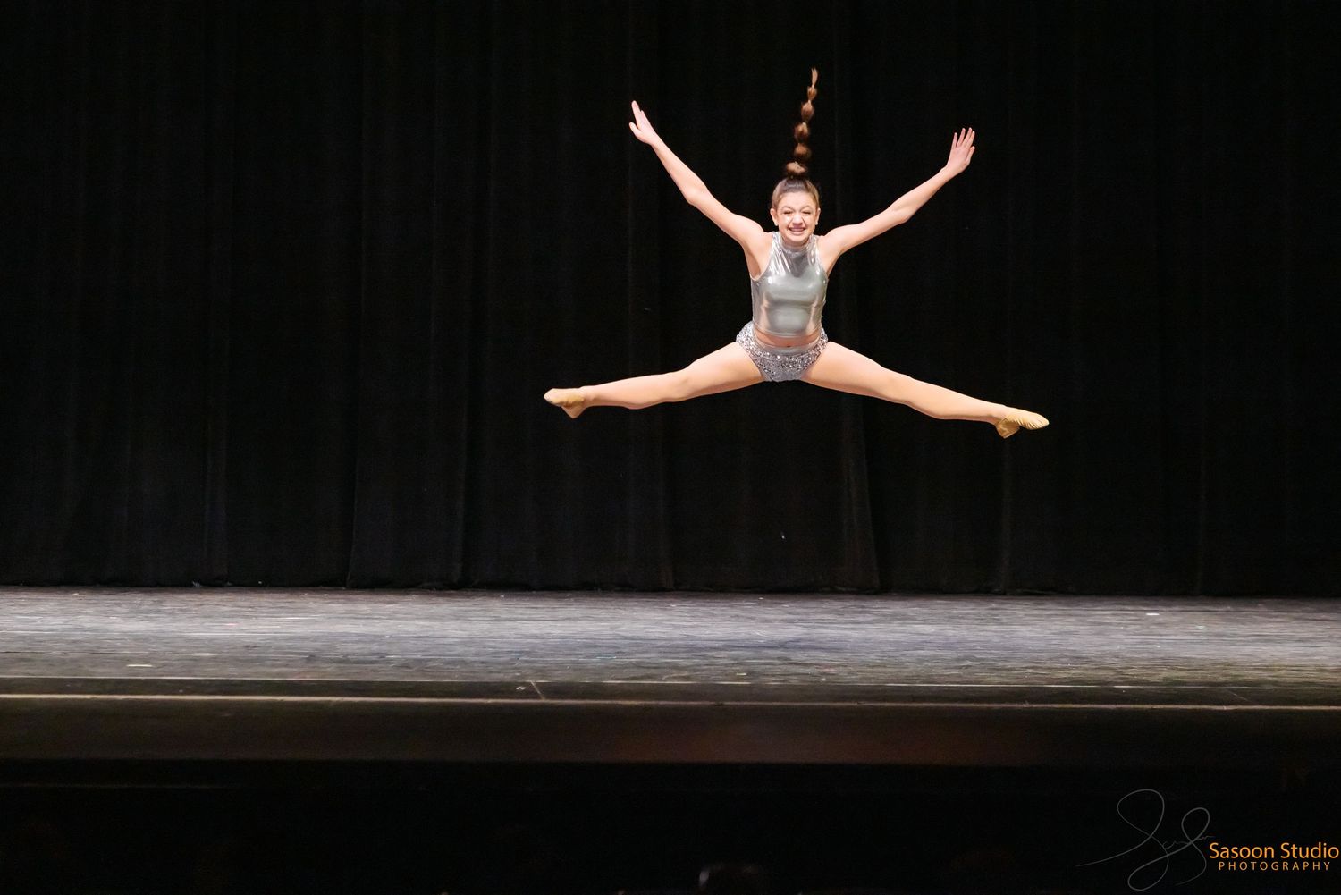 Dancer performs a dramatic split jump in mid-air on a dimly lit stage.