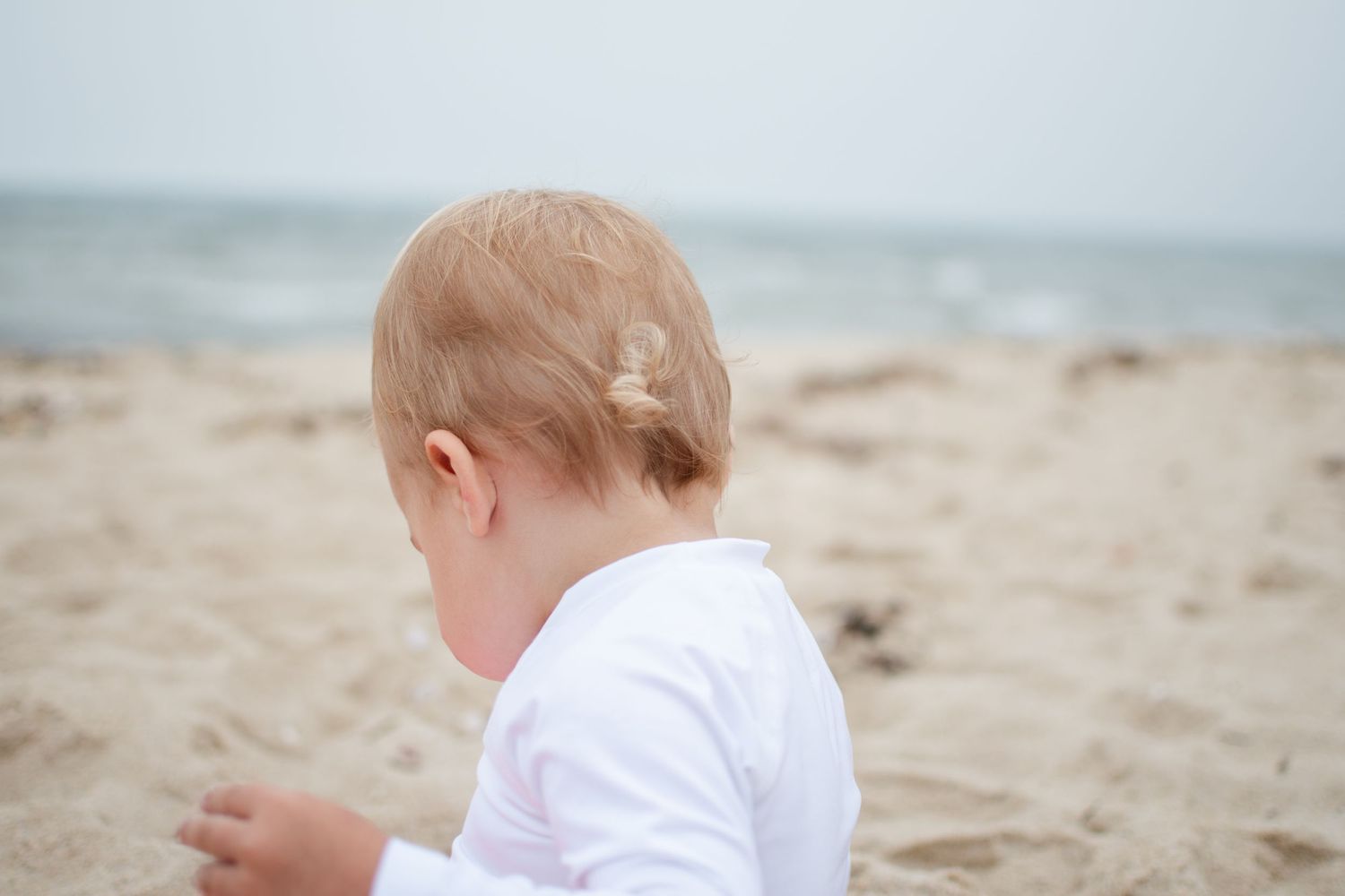 Young boy sits by the ocean on his family's summer vacation.