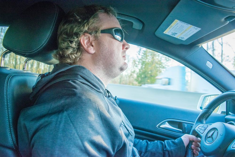 Person wearing sunglasses driving a car on a sunny day.