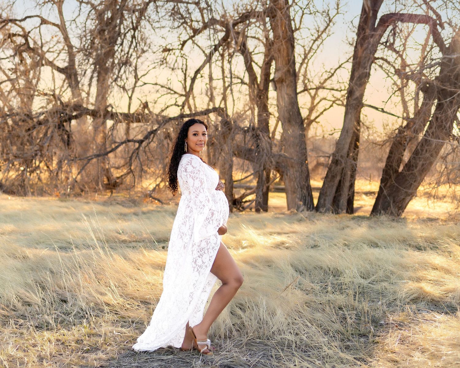 parker maternity photographer.  Pregnant woman in long white dress stood in front of trees, side profile, smiling