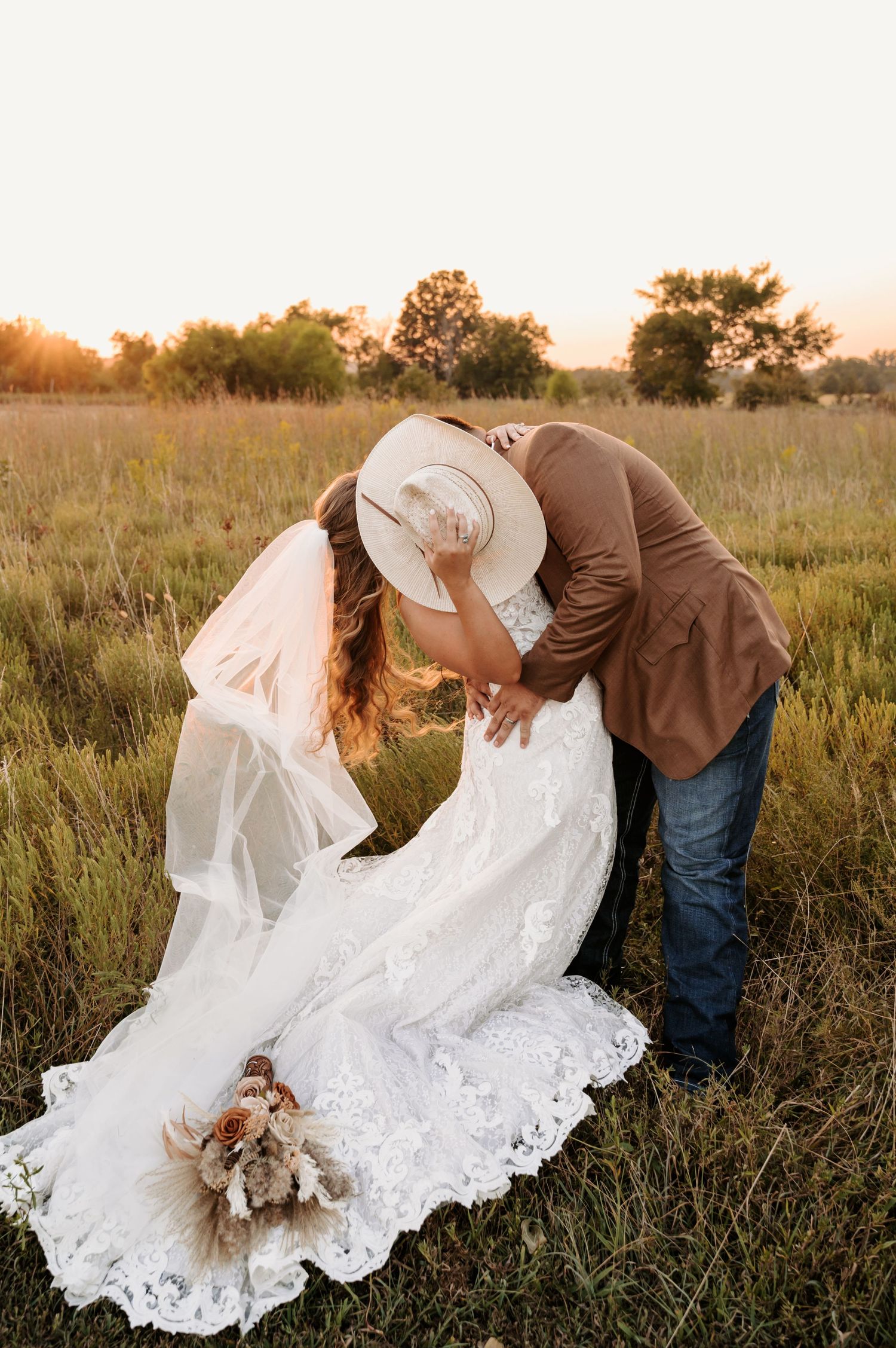 Romantic couple in wedding attire embracing in golden meadow at sunset. Oklahoma Wedding Photographer
