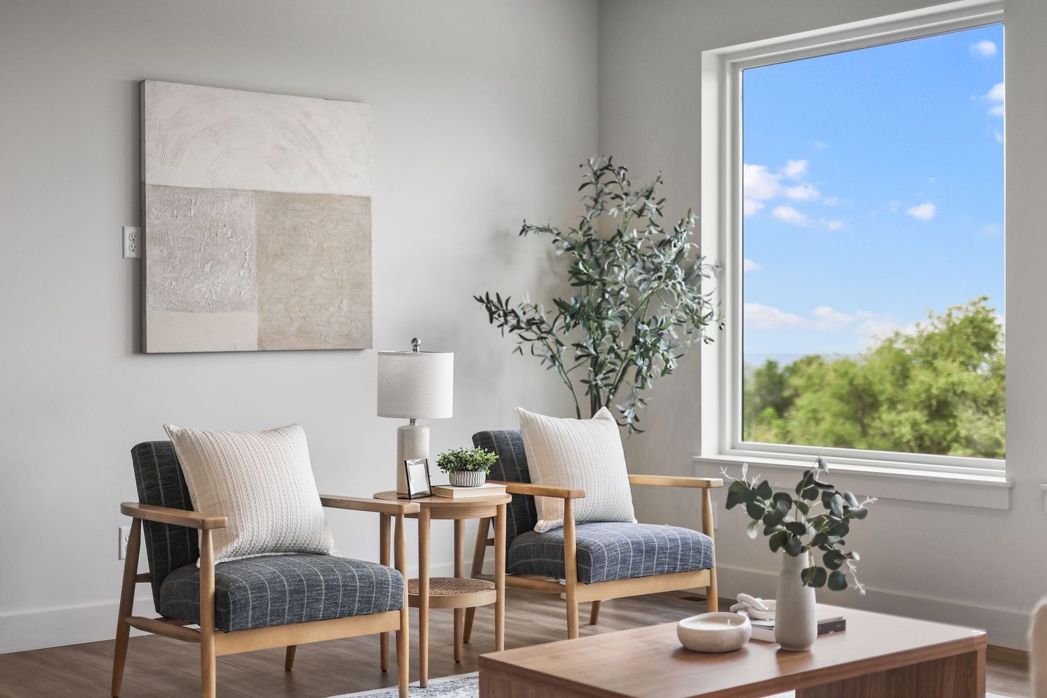 Bright sitting room with two blue chairs, wood coffee table, large window, and indoor plant. Captured by Slate Media (best in UT)