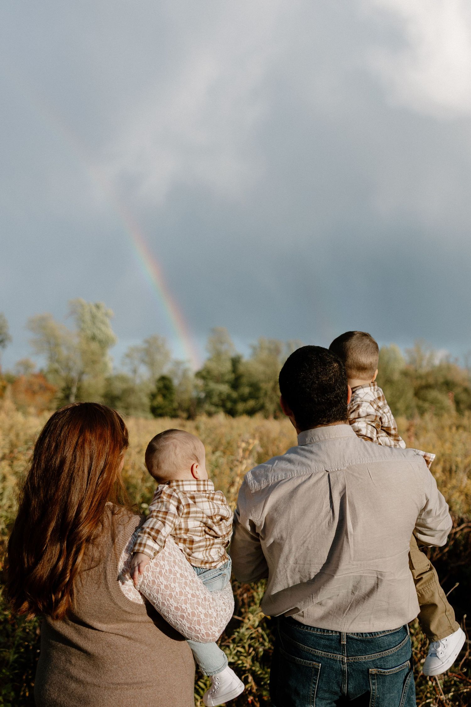 A joyful moment captured outdoors as a baby wearing brown is lifted up in the air during autumn.